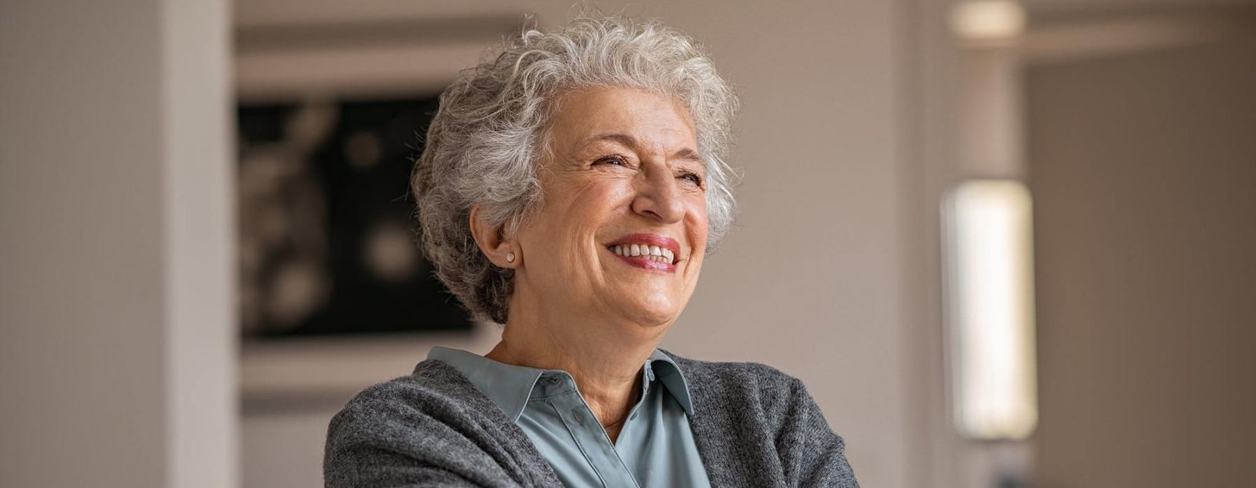 elderly woman with a cane, sits in a room and smiles